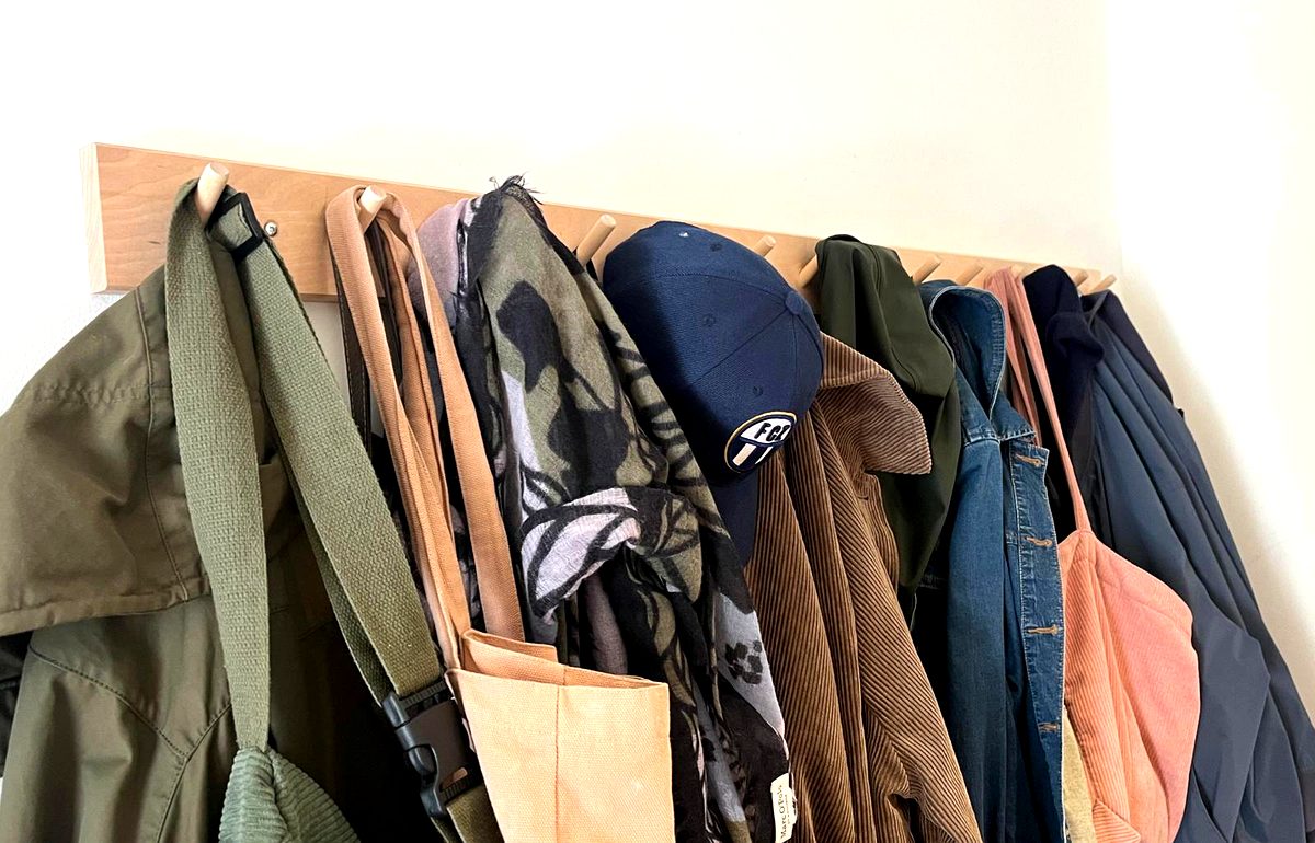 Wooden coat rack mounted on wall with jackets and hats